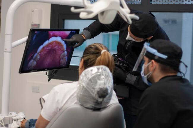 three dentist examine patient mouth diagnosed with Gum Disease on the tv screen 