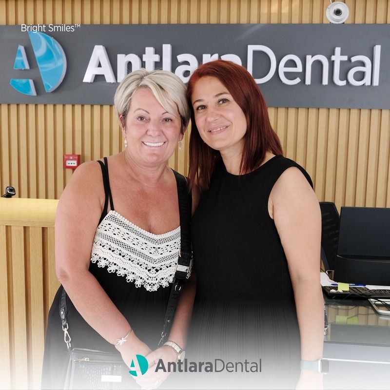 dentist and patient smiles in front of dental clinic logo