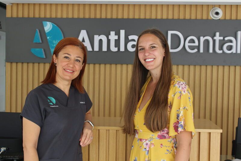 two pretty women smiles in front of antlara dental clinic logo