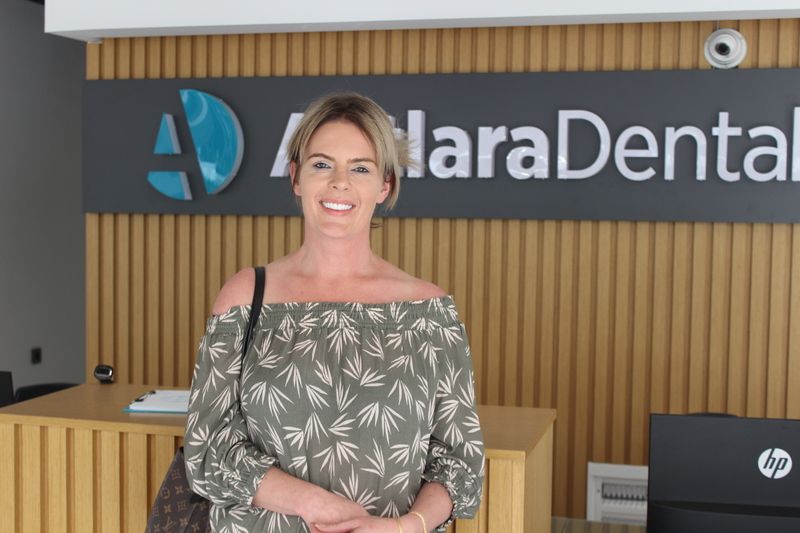 patient having porcelain veneers  stands and smiles in front of Antlara Dental clinic logo